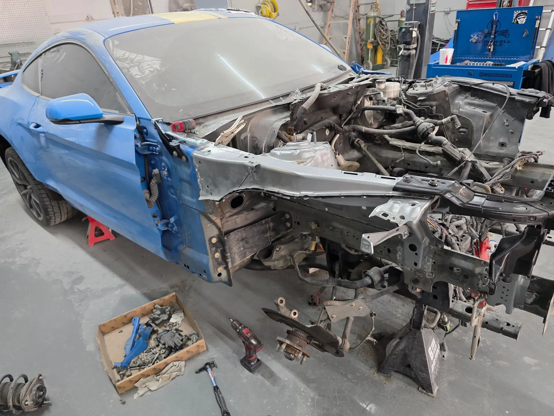 Mechanic working on the rear fender of a dark gray car in a repair shop.