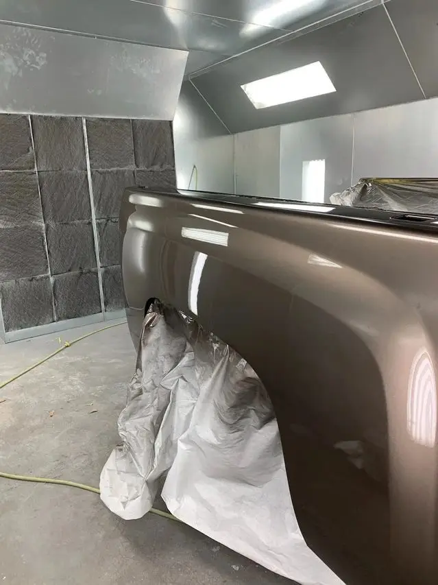 Truck bed being painted in a paint booth; brown paint, bright lighting, gray walls.
