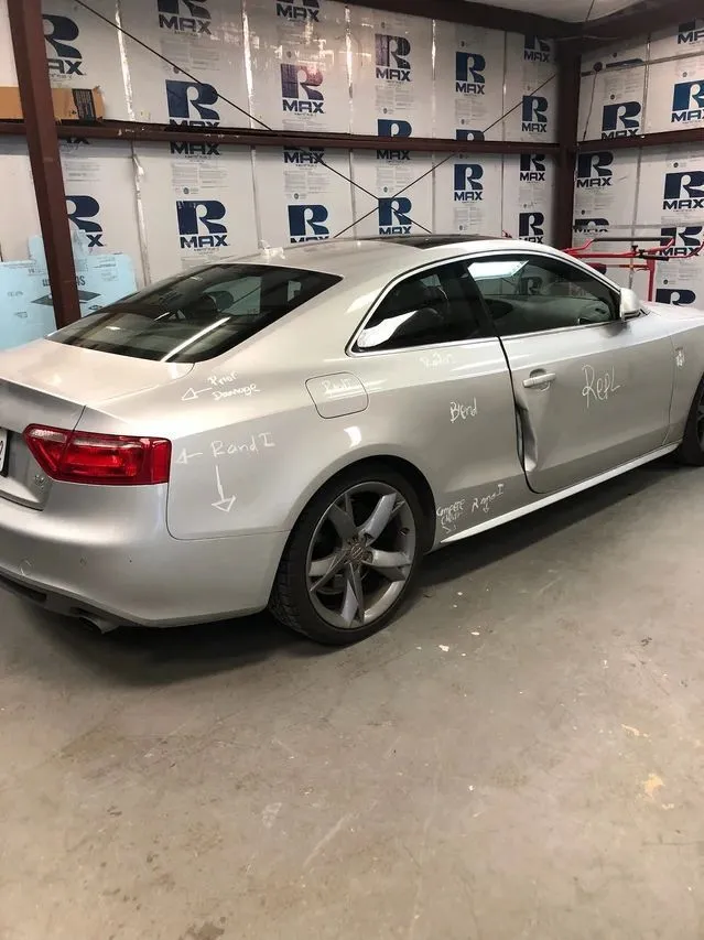 Silver Audi coupe with door damage in a repair shop.