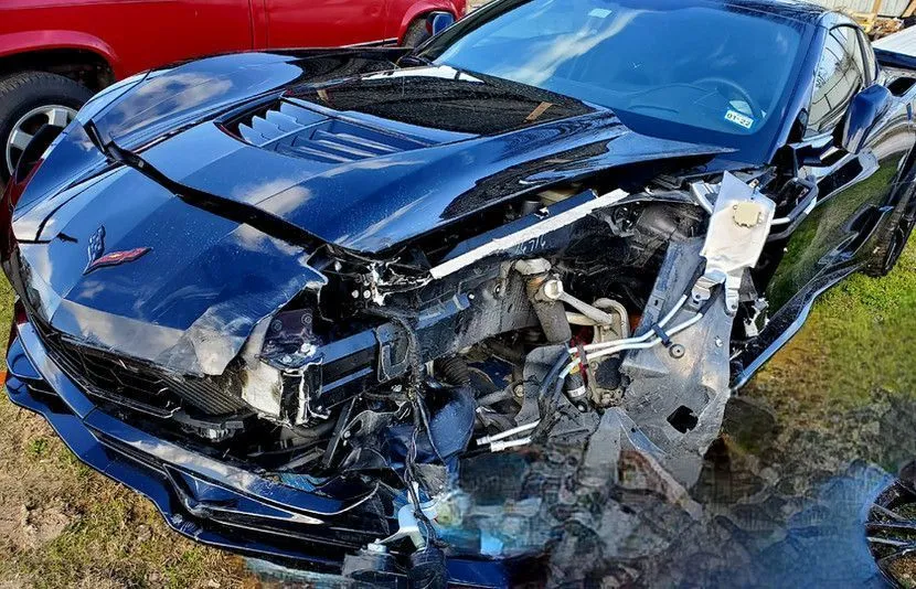 Damaged black Corvette, front-end collision, crumpled hood and body.