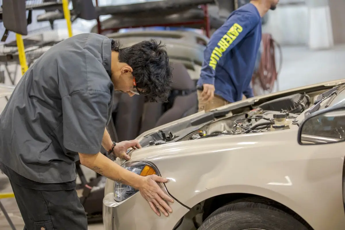Auto body technician checking fender and headlight fit on a car in the shop