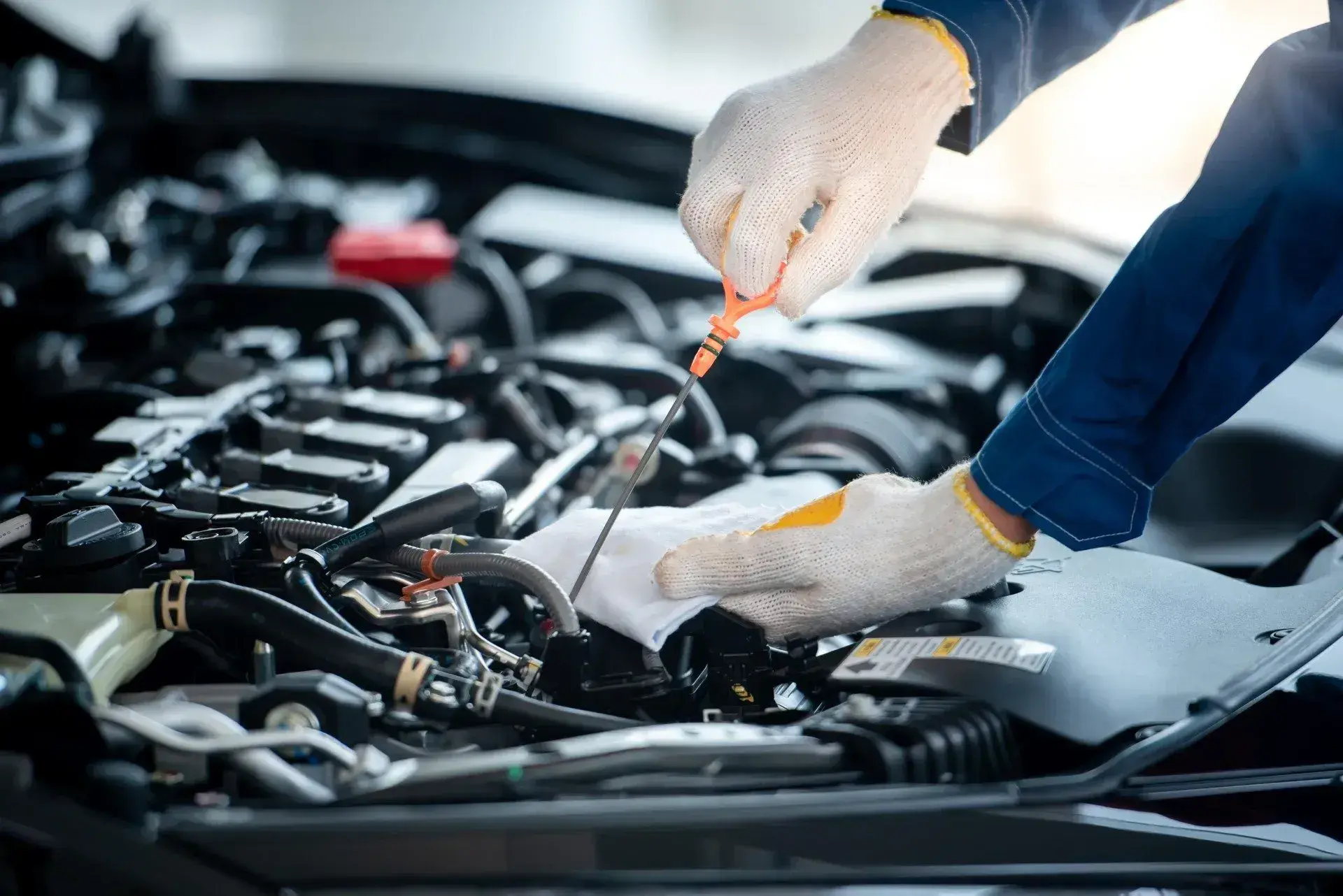 Gloved mechanic checking the engine oil dipstick under the hood of a car