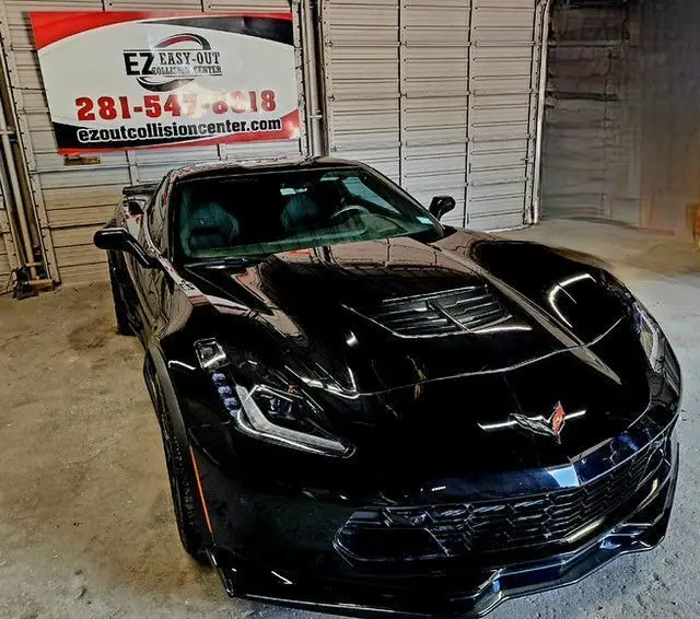 Repaired black Corvette facing forward beneath the Easy Out Collision Center banner