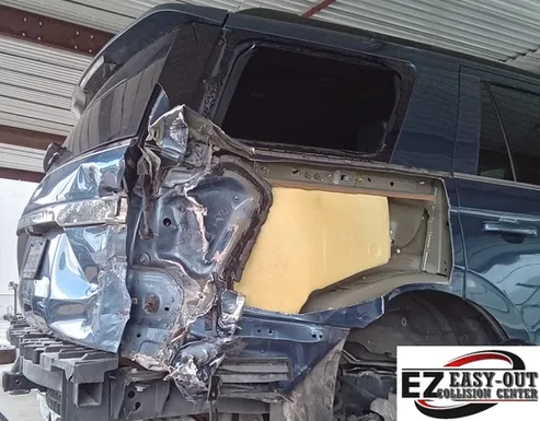 Damaged blue SUV rear with crushed panel, missing window, in a collision repair shop.