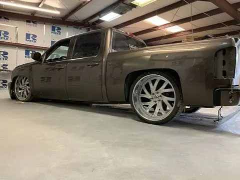 Brown lowered pickup truck with large silver wheels in a garage.