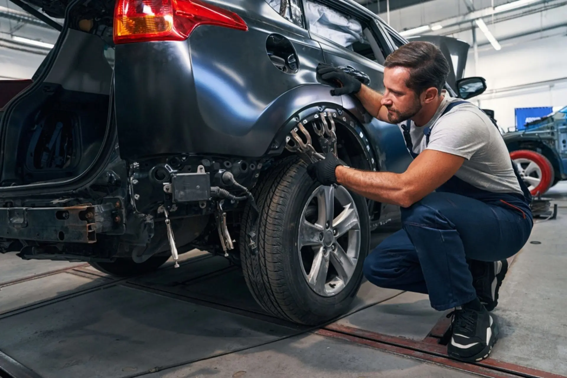Technician working on the rear wheel and fender of a dark SUV in a repair bay