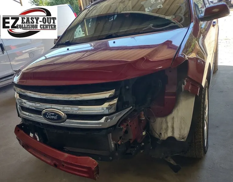 Damaged red Ford Edge missing front bumper and fender at a collision repair center.