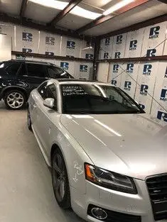 Silver Audi coupe and black SUV parked inside a garage with white and blue insulated walls.