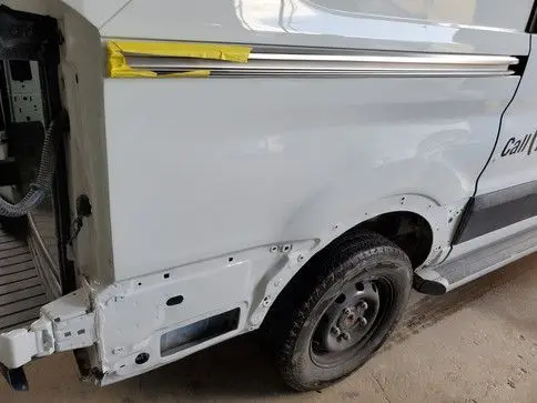 White van with dented rear quarter panel being repaired at a shop, showing new paint.
